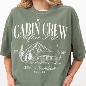May include: A green t-shirt with white text that reads 'Cabin Crew before I do Est. 2025 Katie's Bachelorette Lake Tahoe' with a cabin and trees illustration.