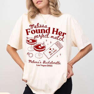May include: Ivory t-shirt with red text that reads "Melissa Found Her Perfect Match" with a graphic of two martini glasses, a box of matches with the text "M+T Est. 2020", and a ring. The text "Melissa's Bachelorette Las Vegas 2025" is also included.