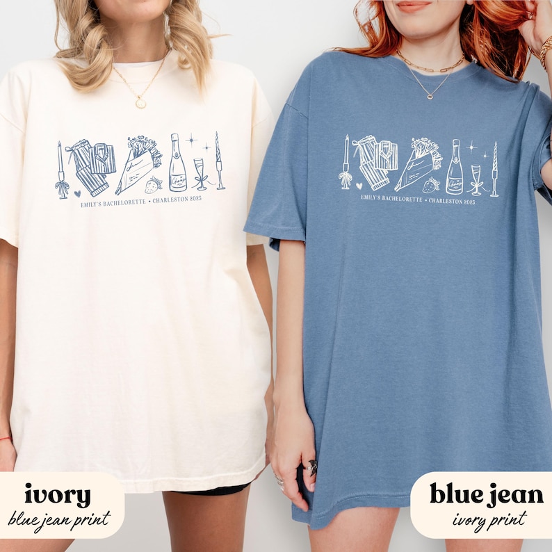 May include: Two t-shirts, one ivory and one blue jean, featuring a white graphic design. The design includes illustrations of a bouquet, champagne bottle, and other celebratory elements. Text on the shirts reads "EMILY'S BACHELORETTE + CHARLESTON 2015".