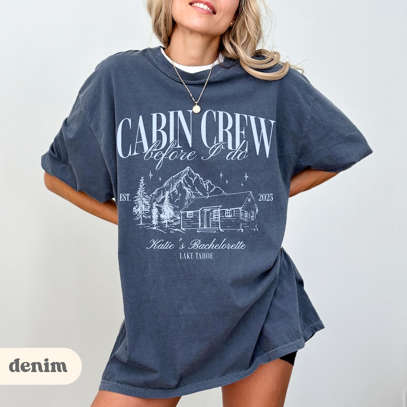 May include: A denim-coloured oversized t-shirt featuring the white text "CABIN CREW before I do". The design includes a cabin, mountains, and trees. The text "Katie's Bachelorette Lake Tahoe" is also printed on the shirt.