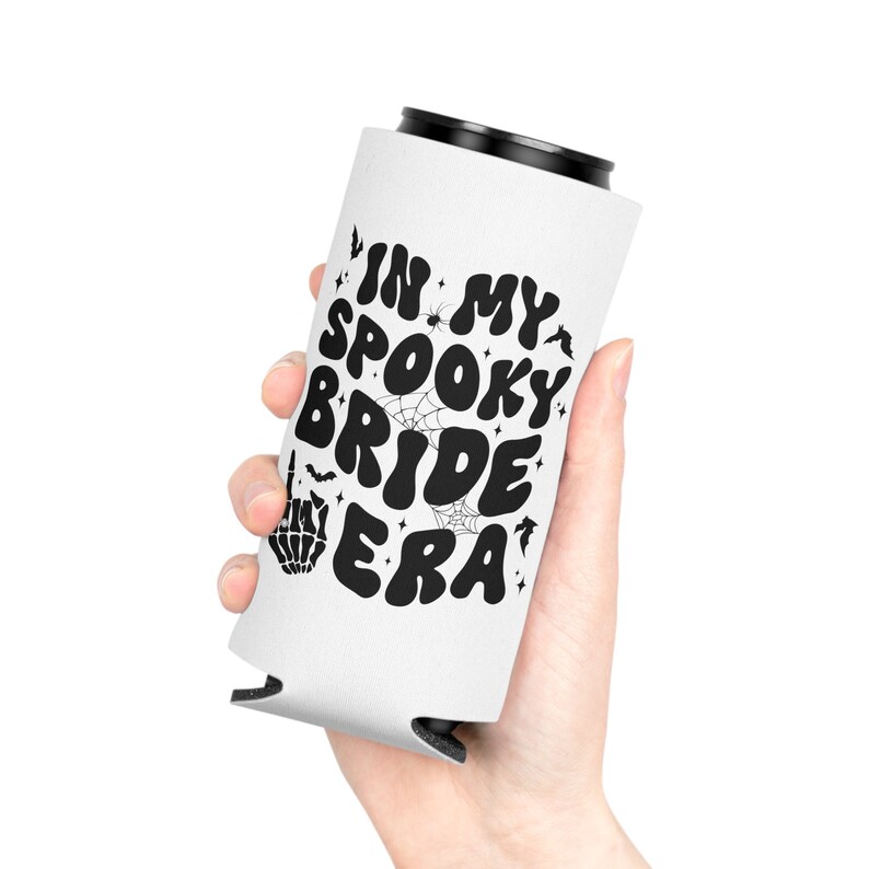 May include: White can cooler with black text that reads "In My Spooky Bride Era". The text is in a retro font with spiderwebs and bats surrounding it.