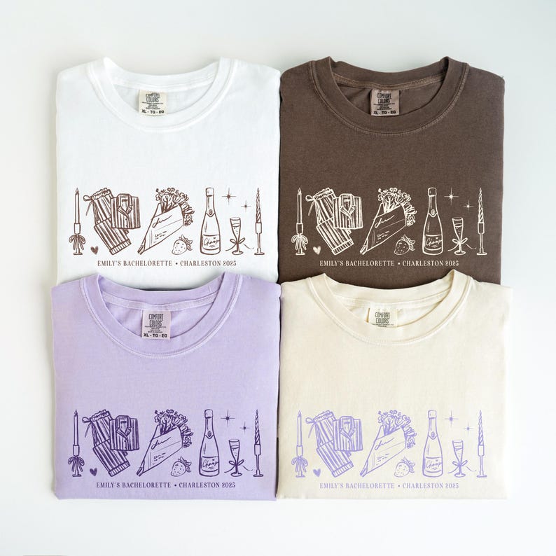 May include: Four t-shirts in white, brown, lavender, and cream, each featuring a line drawing of a champagne bottle, glasses, gifts, flowers, and candles. The text "EMILY'S BACHELORETTE &bull; CHARLESTON 2025" is printed below the design.