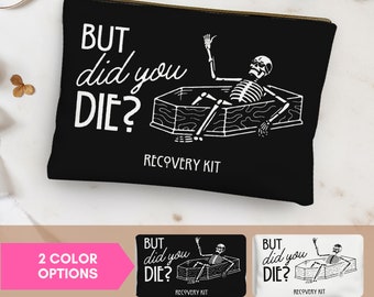 May include: Black canvas zippered pouch with a white graphic of a skeleton in a coffin. The text "BUT did you DIE? RECOVERY KIT" is printed on the pouch.
