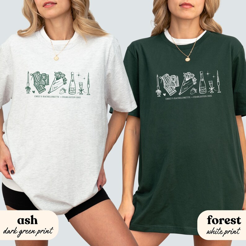 May include: Two t-shirts, one ash gray and one forest green, each with a white graphic design. The design includes illustrations of candles, gifts, flowers, champagne, and glasses. The text "EMILY'S BACHELORETTE - CHARLESTON 2023" is printed below the graphic.