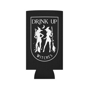 Puede incluir: Enfriador de latas negro con un gr&aacute;fico blanco de dos brujas, estrellas y el texto "DRINK UP WITCHES". El dise&ntilde;o est&aacute; encerrado en un borde blanco. El enfriador est&aacute; dise&ntilde;ado para mantener las bebidas fr&iacute;as.