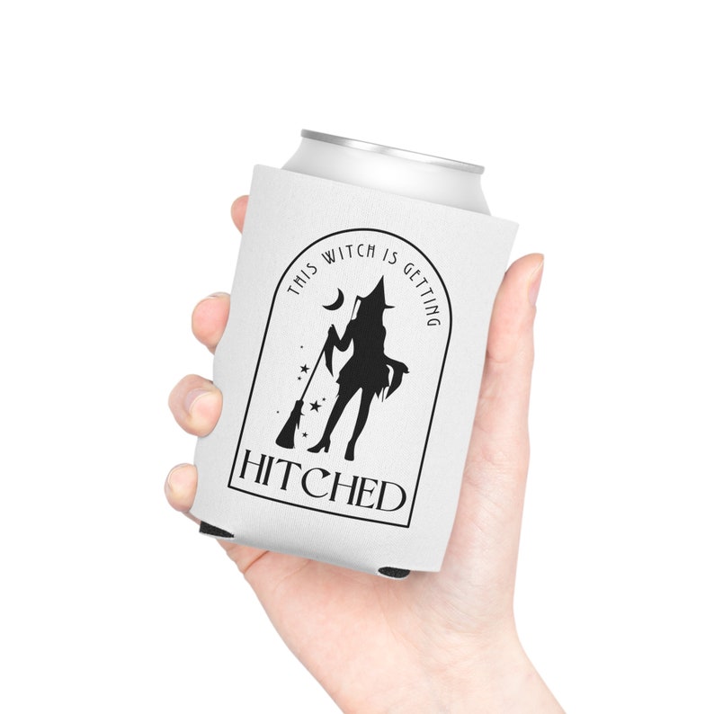 Puede incluir: Enfriador de latas blanco con una silueta negra de una bruja sosteniendo una escoba, una luna y estrellas. El texto "THIS WITCH IS GETTING HITCHED" est&aacute; en un dise&ntilde;o arqueado negro. El enfriador de latas es sostenido por una persona.