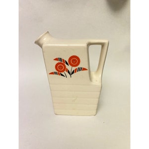 May include: White ceramic jug with a rectangular body and a handle. The jug has a floral design with orange and black flowers.