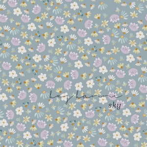 Könnte beinhalten: Nahtloses Blumenmuster mit kleinen weißen, lavendelfarbenen und gelben Blüten auf hellblau-grauem Hintergrund. Der Text "hey hannah sky" befindet sich unten rechts. Geeignet für Textilien und Tapeten.