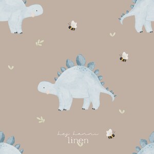 Könnte beinhalten: Wiederholendes Aquarellmuster mit hellblauen Dinosauriern, Bienen und Zweigen auf beigem Hintergrund. Der Text "hey hanni linen" befindet sich unten rechts. Geeignet für Kinderprodukte.