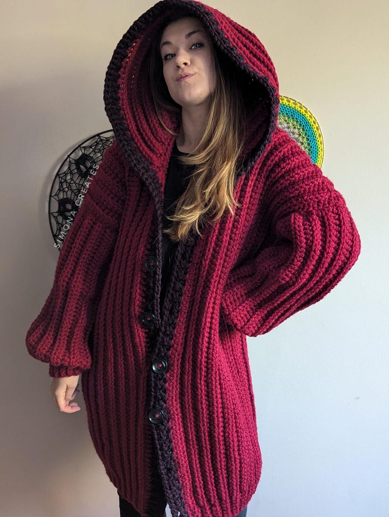 Pu&ograve; includere: Un lungo cardigan in crochet color borgogna con bordino nero e cappuccio. Il cardigan ha una chiusura con bottoni ed &egrave; realizzato con un filato spesso.