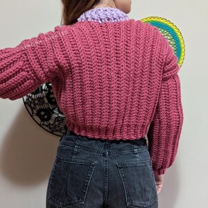 Pu&ograve; includere: Un maglione rosa lavorato a uncinetto con maniche lunghe e una lunghezza corta. Il maglione &egrave; realizzato con un punto testurizzato e ha una vestibilit&agrave; rilassata.