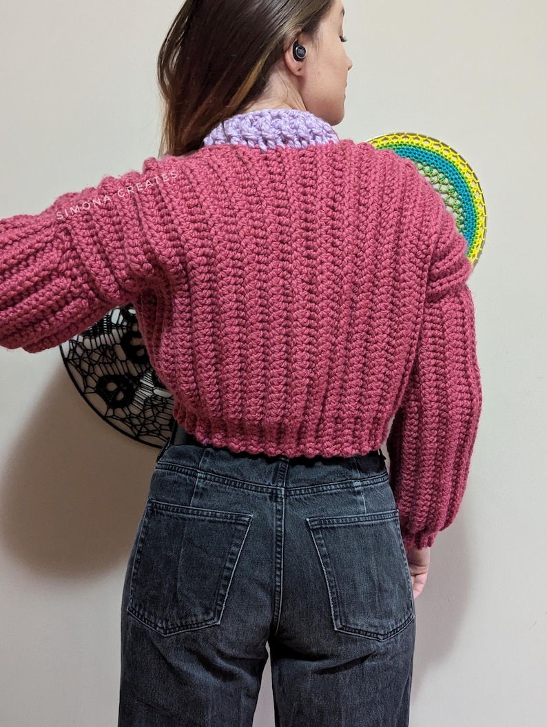 Pu&ograve; includere: Un maglione rosa lavorato a uncinetto con maniche lunghe e una lunghezza corta. Il maglione &egrave; realizzato con un punto testurizzato e ha una vestibilit&agrave; rilassata.