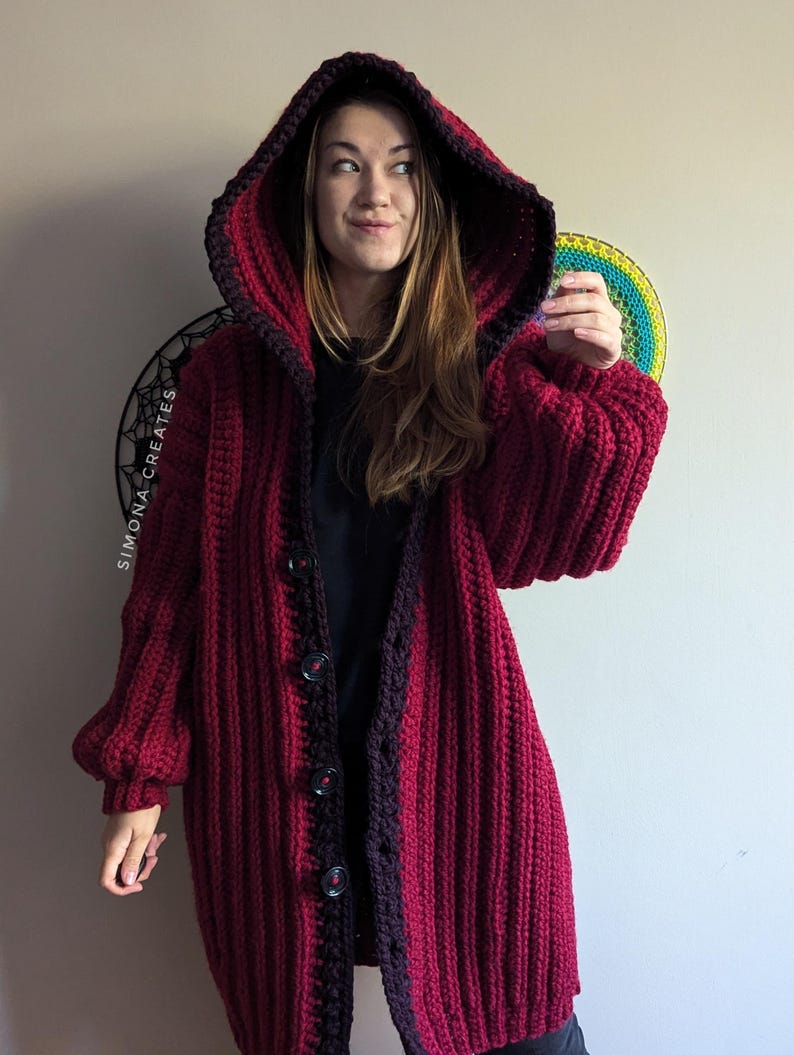 Pu&ograve; includere: Un lungo cardigan in crochet color borgogna con bordino nero e cappuccio. Il cardigan ha una chiusura con bottoni ed &egrave; realizzato con un filato spesso.