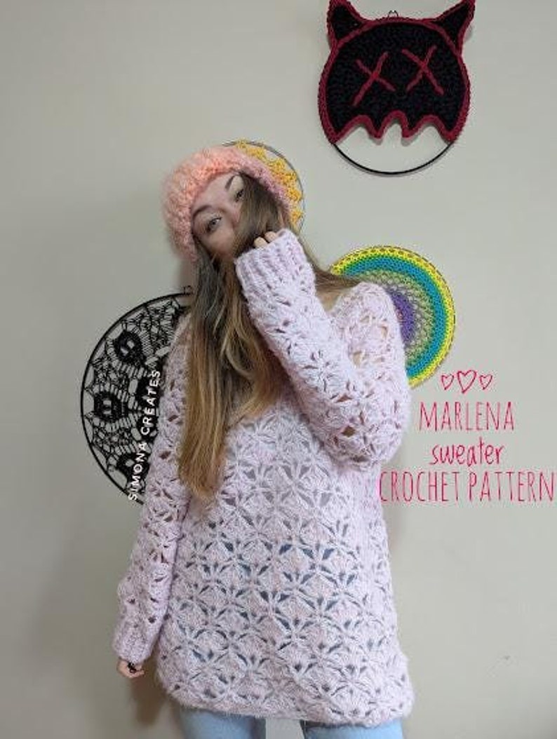 May include: A pink crochet sweater with a lacy pattern. The sweater is being modeled by a person wearing a pink and orange crocheted hat and blue jeans. The text "Marlena sweater crochet pattern" is visible in the image.