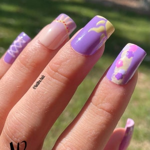 May include: Purple and pink short square-shaped acrylic nails with a sun and flower design.