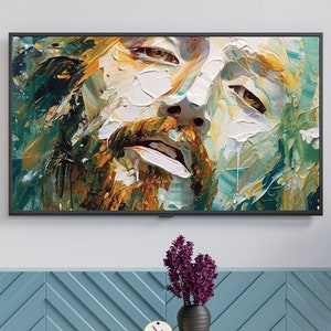 May include: A framed abstract painting of a man's face with a textured, brushstroke style. The painting is in shades of blue, green, yellow, and brown. The painting is hanging on a wall above a blue cabinet with a white clock on a wooden table.