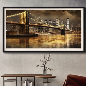 May include: A nighttime view of the Brooklyn Bridge in New York City, with the Manhattan skyline in the background. The bridge is lit up with golden lights, and the water below is reflecting the city lights.