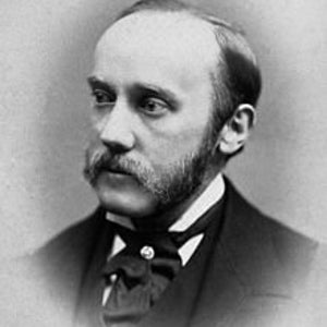 May include: A black and white portrait photograph of a man with a moustache and beard. He is wearing a dark suit and a white shirt with a bow tie.