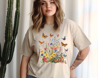 May include: A beige t-shirt with a colorful floral and butterfly print. The print features a variety of flowers in shades of pink, yellow, blue, and purple, with butterflies in shades of blue, orange, and yellow.