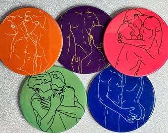 May include: Set of five round coasters with line art illustrations of embracing figures. Each coaster has a different color: orange, purple, pink, green, and blue. The illustrations are in white or gold.