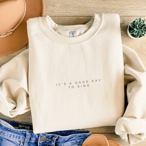 May include: A cream-colored sweatshirt with the text "It's a good day to sing" printed on the front.