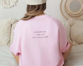 Puede incluir: Sudadera rosa con el texto "Celebrate life with each plie and pirouette" impreso en la espalda.