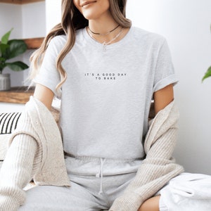 Pode incluir: Uma camiseta cinza com o texto "It's a good day to bake" estampado na frente.