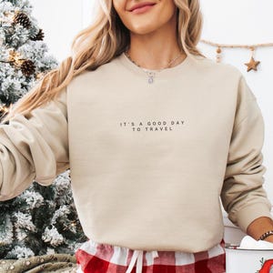 May include: A beige sweatshirt with the text "It's a good day to travel" printed on the front.