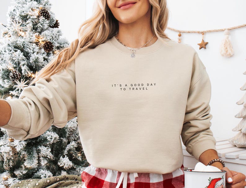 May include: A beige sweatshirt with the text "It's a good day to travel" printed on the front.