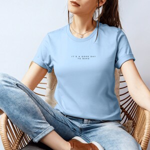 Pode incluir: Uma camiseta azul claro com o texto "It's a good day to bake" impresso na frente.