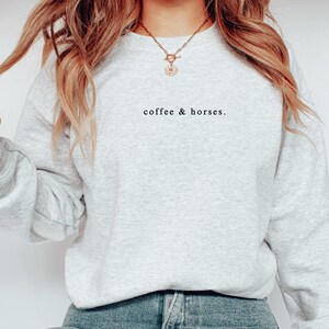 K&ouml;nnte beinhalten: Ein hellgraues Sweatshirt mit dem Text "coffee & horses." in Schwarz. Das lang&auml;rmlige Oberteil mit Rundhalsausschnitt ist aus einem weichen Material gefertigt. Das Sweatshirt hat einen l&auml;ssigen Stil.