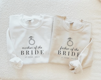 Puede incluir: Dos sudaderas blancas con texto negro y un diseño de anillo. El texto en la sudadera de la izquierda dice "mother of the BRIDE 17 JUNE, 2025". El texto en la sudadera de la derecha dice "father of the BRIDE 17 JUNE, 2025".