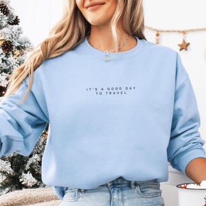 May include: A light blue sweatshirt with the text "It's a good day to travel" printed on the front.