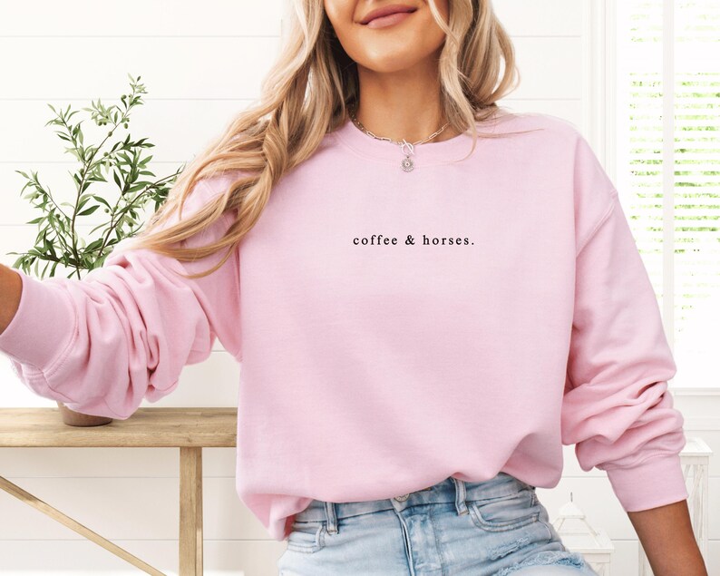 K&ouml;nnte beinhalten: Ein hellrosa Sweatshirt mit dem Text "coffee & horses." in schwarzer Schrift. Das lang&auml;rmlige Oberteil ist aus einem weichen Material gefertigt. Das Sweatshirt ist ein l&auml;ssiger Stil und wird von einer Person getragen.