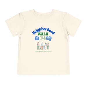May include: A cream-coloured short-sleeve t-shirt featuring a graphic with the text Neighbourhood Walk Club, Join Us, Every Sunday, and A Simple Walk With A Great Community. The design includes a colourful illustration of a group of people walking.