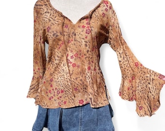 May include: A long-sleeved top featuring a tan and brown animal print pattern with small red floral accents, a V-neckline with thin tie strings, and flared bell sleeves, paired with a blue denim pleated skirt with a visible front seam.