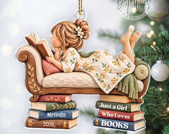 May include: A 2D flat Christmas ornament featuring a girl with brown hair in a floral dress reading a book while lying on a chaise lounge supported by stacks of books. The books are labeled with the text Melinda, 2026, and Just a Girl Who Loves BOOKS.