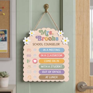 May include: A light-colored wooden hanging sign with scalloped edges, featuring the text Mrs. Brooks School Counselor. It includes six status options with colored bars: In a Meeting, In a Classroom, Come on In, With a Student, Out of Office, and At Lunch.
