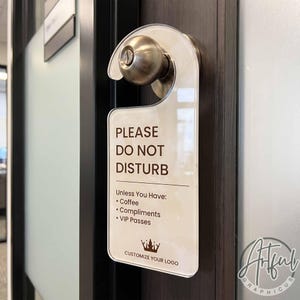 May include: A clear acrylic door hanger with brown text that reads: PLEASE DO NOT DISTURB. Unless You Have: Coffee, Compliments, VIP Passes. Below the text is a crown icon and the words CUSTOMIZE YOUR LOGO. The hanger is hooked onto a metal doorknob.