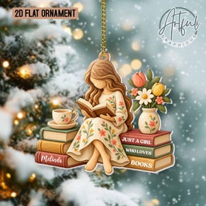 May include: A 2D flat ornament featuring a girl with long brown hair reading a book while sitting on a stack of books. The ornament includes a cup on a saucer, a vase of flowers, and the text "JUST A GIRL WHO LOVES BOOKS" and "Melinda".
