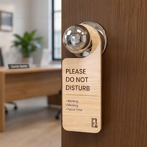 May include: A light wood door hanger with a circular cutout hanging on a silver doorknob. The text reads: PLEASE DO NOT DISTURB, followed by Working, Meeting, and Focus Time, with a small icon of a door with a lock at the bottom of the sign.