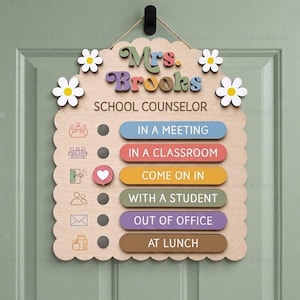 May include: A scalloped wooden door sign for a school counselor named Mrs. Brooks. It features a sliding heart indicator next to status options: In a Meeting, In a Classroom, Come On In, With a Student, Out of Office, and At Lunch, with floral accents.