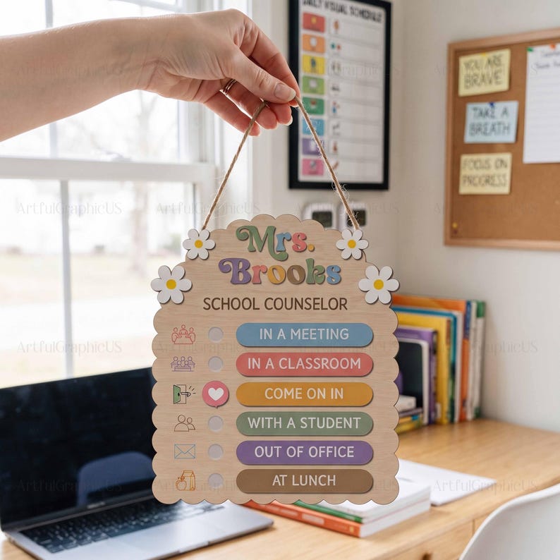 May include: A light-colored wooden sign with scalloped edges and white flower accents. The text reads Mrs. Brooks SCHOOL COUNSELOR. It features a list of status options including IN A MEETING, IN A CLASSROOM, COME ON IN, WITH A STUDENT, OUT OF OFFICE, and AT LUNCH.