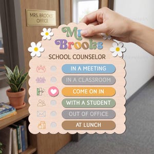May include: A scalloped wooden sign featuring the text "Mrs. Brooks SCHOOL COUNSELOR" with white daisy accents. It includes a status tracker with options: IN A MEETING, IN A CLASSROOM, COME ON IN, WITH A STUDENT, OUT OF OFFICE, and AT LUNCH.