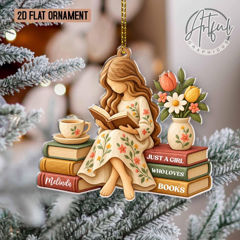 May include: A 2D flat ornament featuring a figure with long hair wearing a floral dress, reading a book while sitting on a stack of books. The ornament includes a vase of flowers, a teacup, and text that reads "JUST A GIRL WHO LOVES BOOKS" and "Melinda".