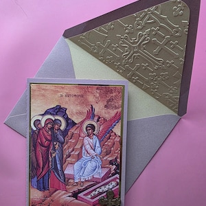 Może przedstawiać: Religijna kartka z życzeniami z ikonograficznym obrazem i tekstem, prezentowana w ozdobnej kopercie. Koperta ma wytłoczony złoty wzór krzyża. Do kartki przymocowany jest mały metalowy krzyż.
