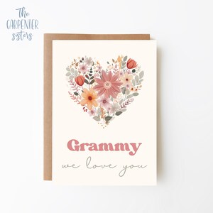 May include: A card with a floral heart design in shades of pink, orange, and green. The text "Grammy we love you" is written in a pink retro font.