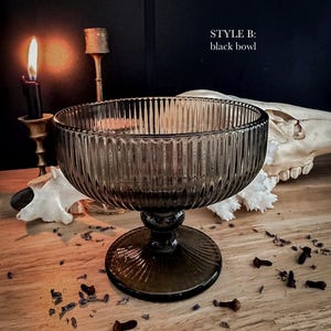 K&ouml;nnte beinhalten: Eine durchscheinende schwarze Glasschale mit vertikalem Rillenmuster, ausgestattet mit einem breiten kreisf&ouml;rmigen Rand, einem kurzen Stiel und einem runden Fu&szlig;. Der Text "STYLE B: black bowl" ist oben rechts im Bild in Wei&szlig; gedruckt.
