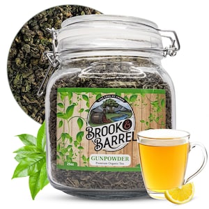 May include: A glass jar filled with green tea leaves, a cup of brewed tea, and a lemon wedge. The jar has a label that reads "Brook & Barrel Gunpowder Premium Organic Tea." A portion of loose tea is displayed in a circle behind the jar.