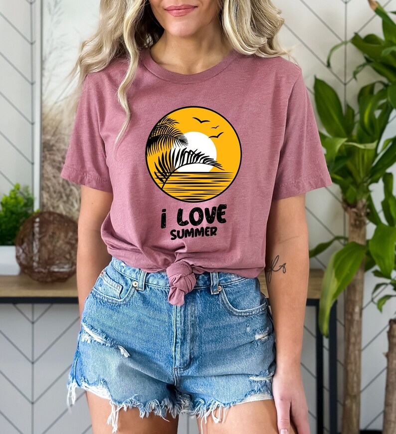 May include: A mauve t-shirt with a yellow circle graphic featuring a palm tree, sun, and birds. The text "i love summer" is printed below the graphic.